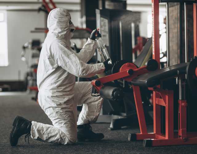 Worker sanitizing gym equipment